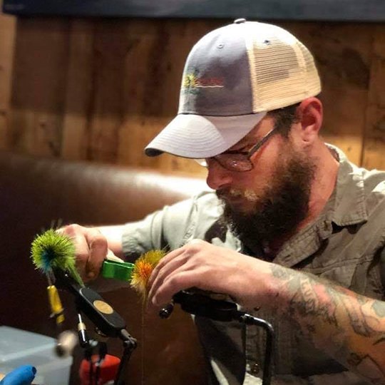 Man sitting working on fly tying and using fly tying supplies