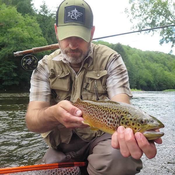 Fisherman using fly tying tools and fishing gear to catch a green and orange spotted fish