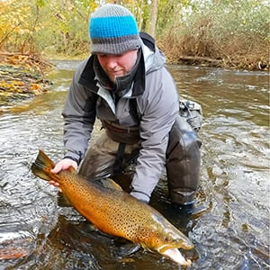 Fisherman holding an orange and yellow fish near a stream